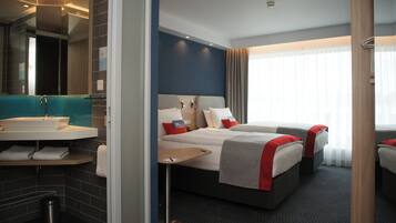 Ein Hotelzimmer mit Bad, einem Bett mit Kissen, einem Nachttisch und einem Fenster mit Vorhängen.