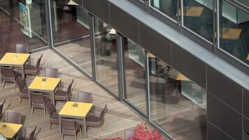 An outdoor seating area with tables and chairs, a potted plant, and a glass railing.