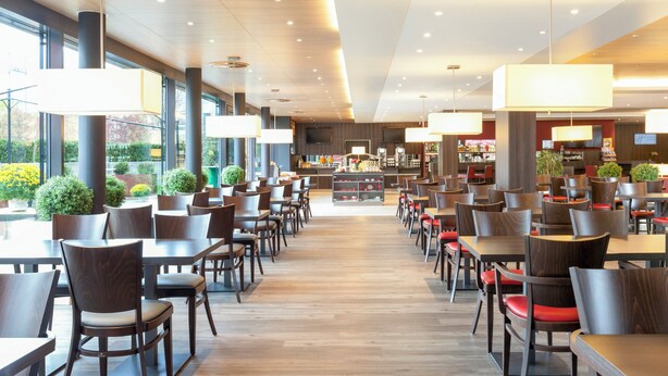 A spacious restaurant with high ceilings, modern lighting, and a central counter. - Holiday Inn Express Zurich Airport by IHG (Ruemlang)