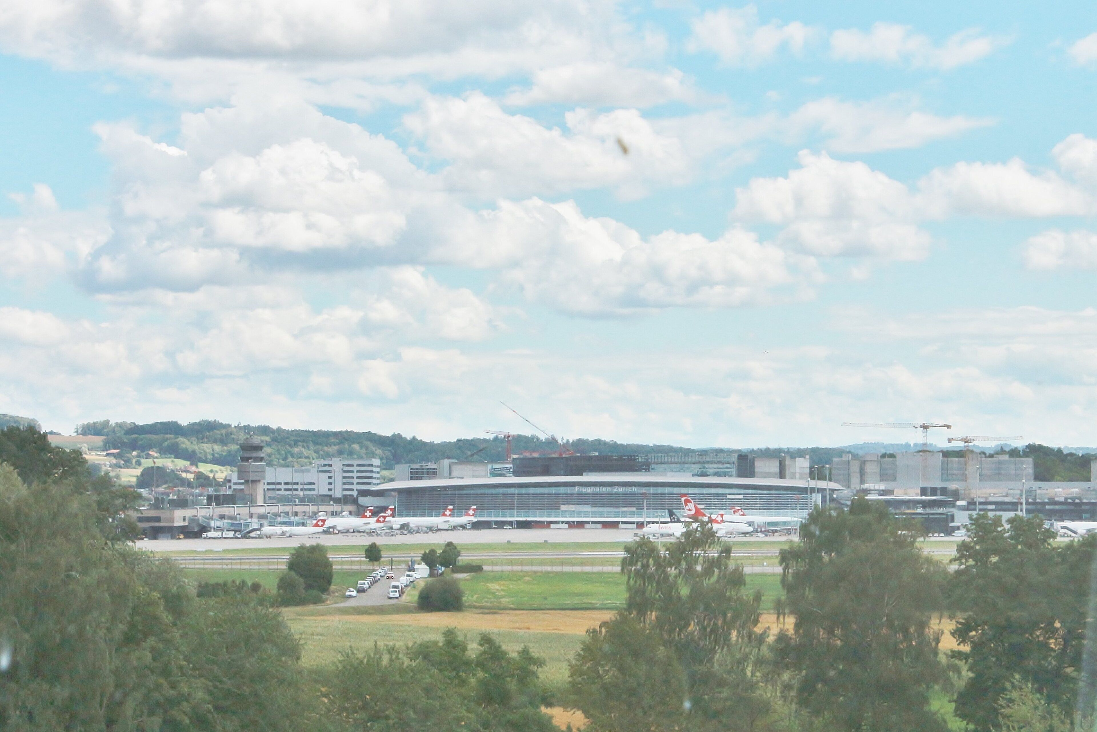 Un aeropuerto con un amplio edificio terminal, aviones estacionados y zonas verdes circundantes.