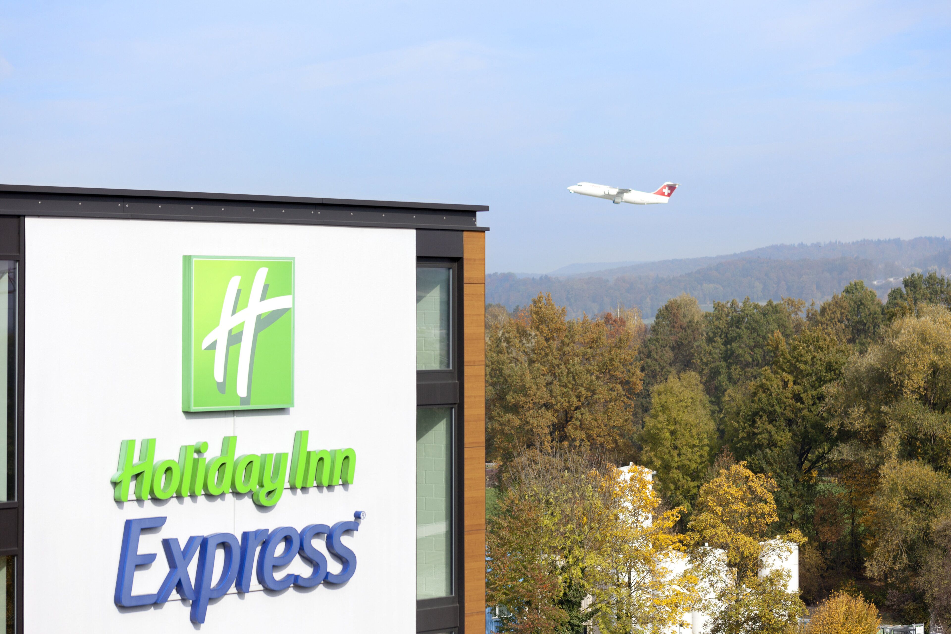 A Holiday Inn Express sign with a view of a forest and a plane in the background.