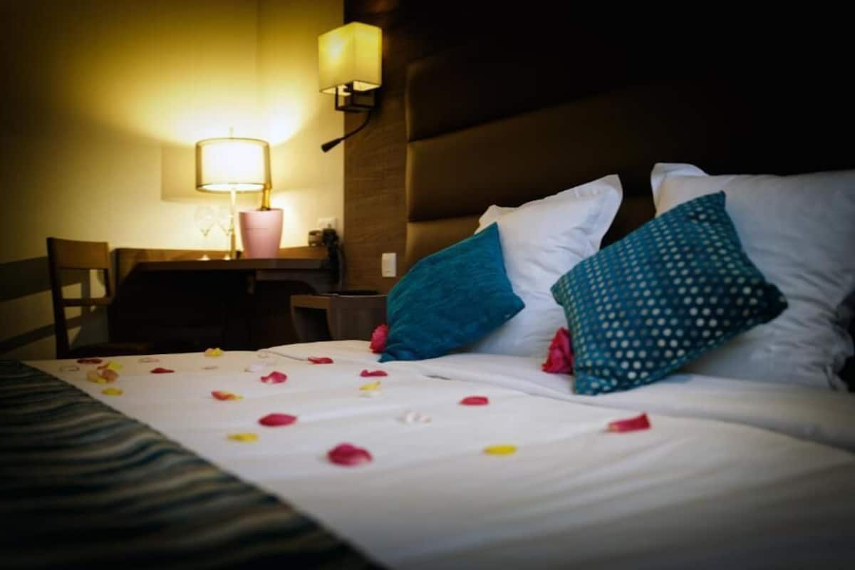 Habitación de hotel con cama, almohadas, mesita de noche, lámpara y una silla.