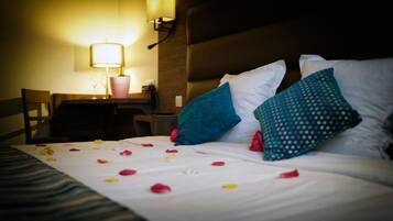 A hotel room with a bed, pillows, a bedside table, a lamp, and a chair.