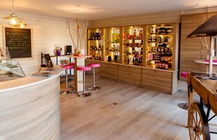 Un área de bar con estantes de madera llenos de botellas, un menú en la pizarra y taburetes de bar color rosa.