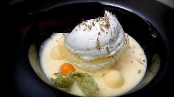 A dessert with a scoop of ice cream on top, garnished with herbs, served in a bowl with a sauce and a cherry.