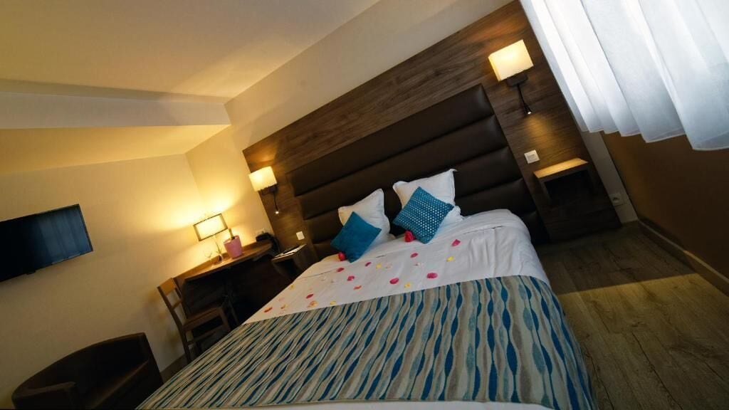 A hotel room with a large bed, two bedside tables with lamps, a flat-screen TV mounted on the wall, and a wooden floor.
