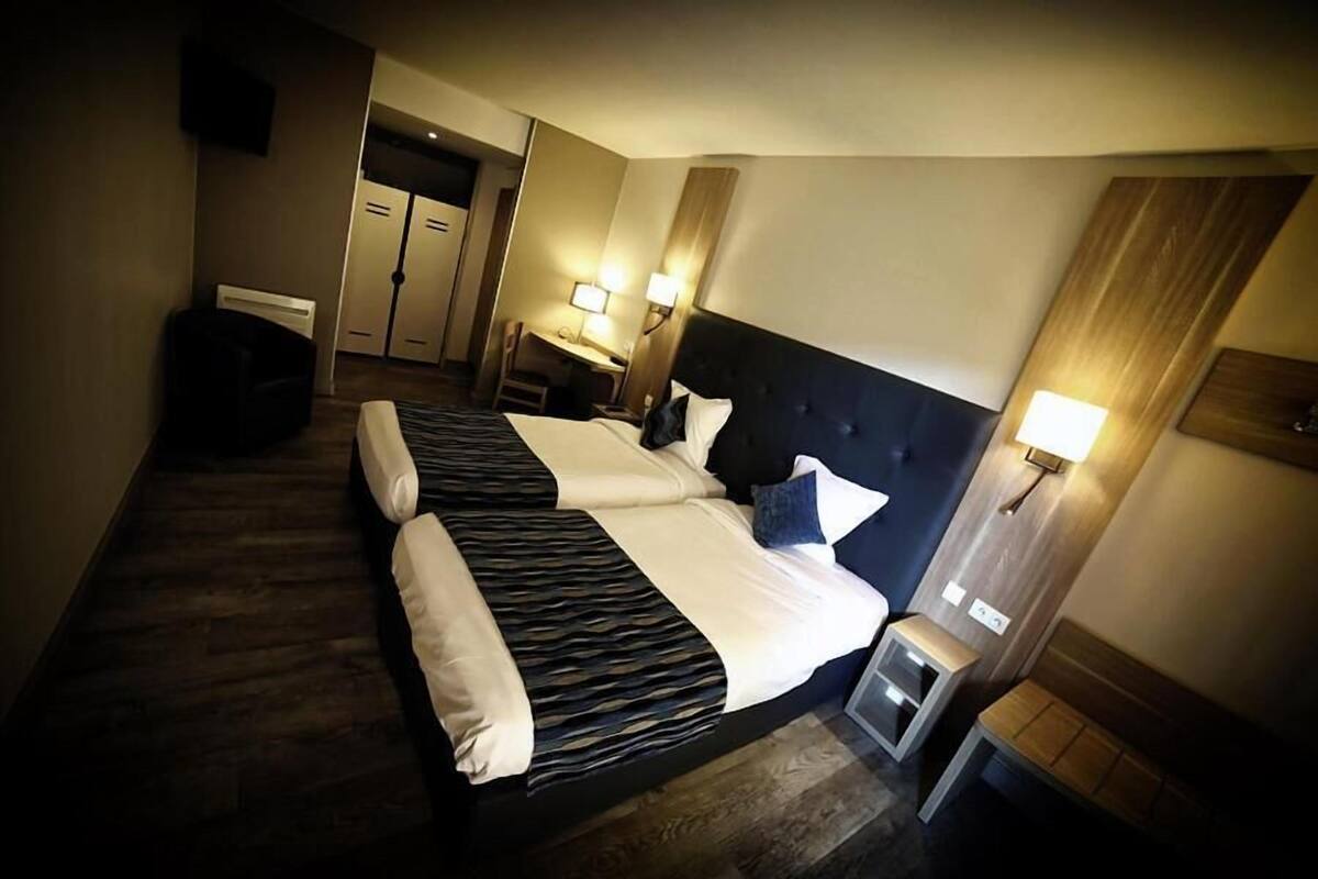 Una habitación de hotel con una cama grande, mesitas de noche, lámparas y un armario.