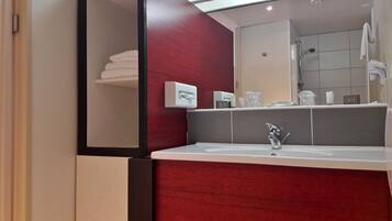 Une salle de bain moderne avec un grand miroir, un lavabo et un espace douche.