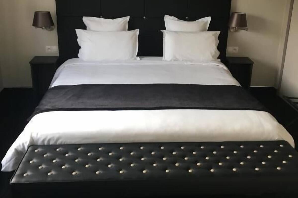 Una cama bien tendida, con tablero cabecera negro y ropa de cama blanca.