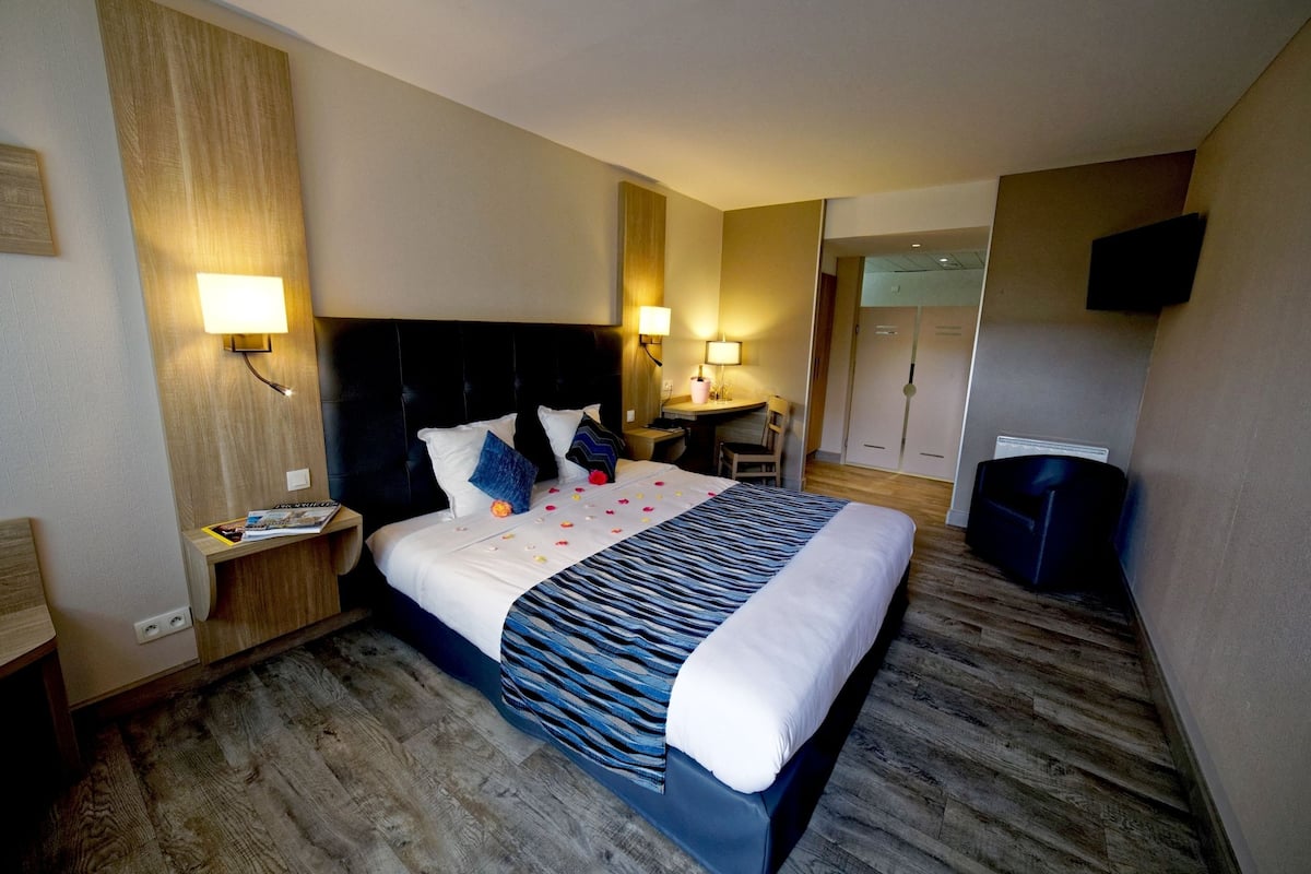 Habitación de hotel con una cama grande, mesitas de noche, un escritorio, una silla, un televisor y un armario.