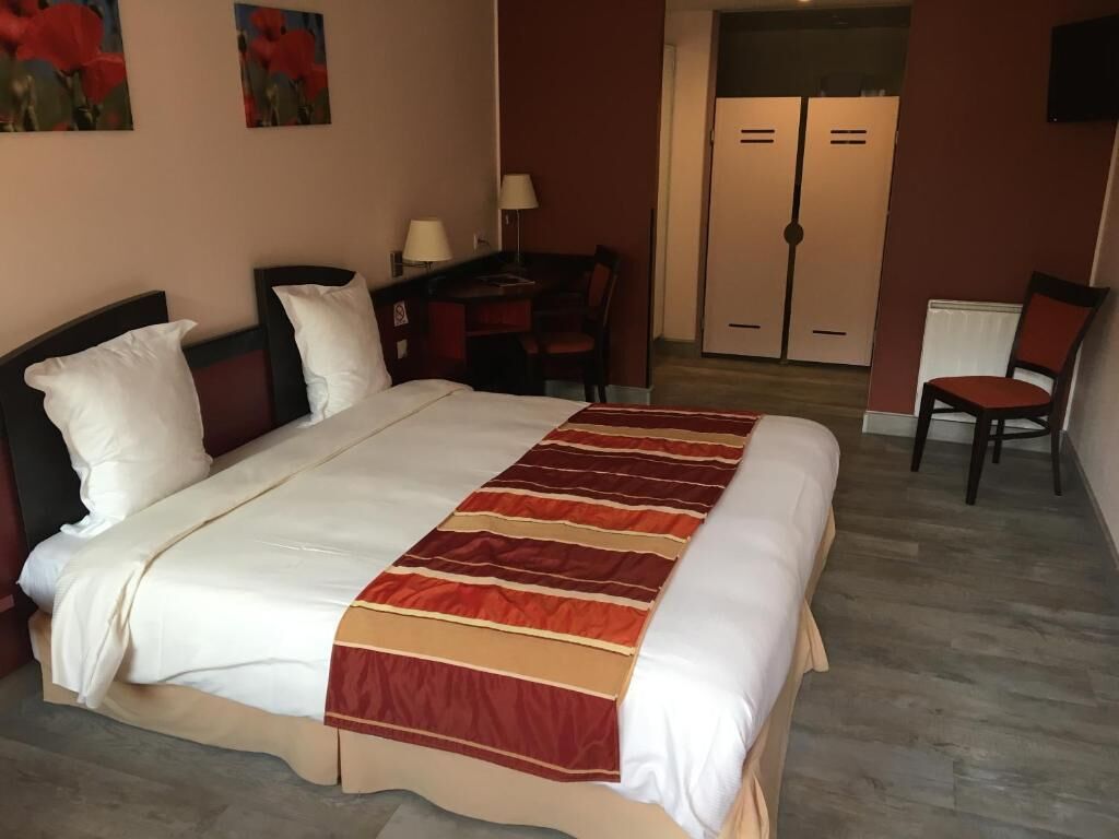 Habitación de hotel con una cama grande, un escritorio con silla, un armario y un televisor montado en la pared.