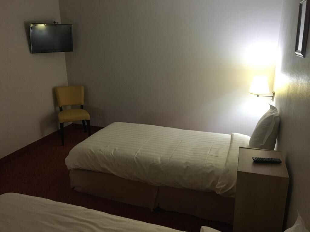 Une chambre d’hôtel avec deux lits simples, une chaise, un téléviseur fixé au mur et une table de chevet avec une lampe.