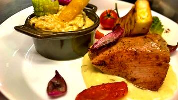 A plate with a piece of meat, a small bowl of sauce, and some vegetables.