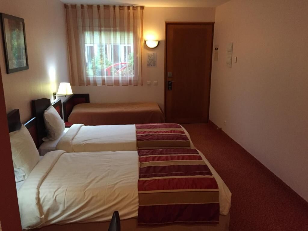 Habitación de hotel con dos camas, una ventana con cortinas, una lámpara de pared y una puerta.