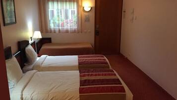 Habitación de hotel con dos camas, una ventana con cortinas, una lámpara de pared y una puerta.