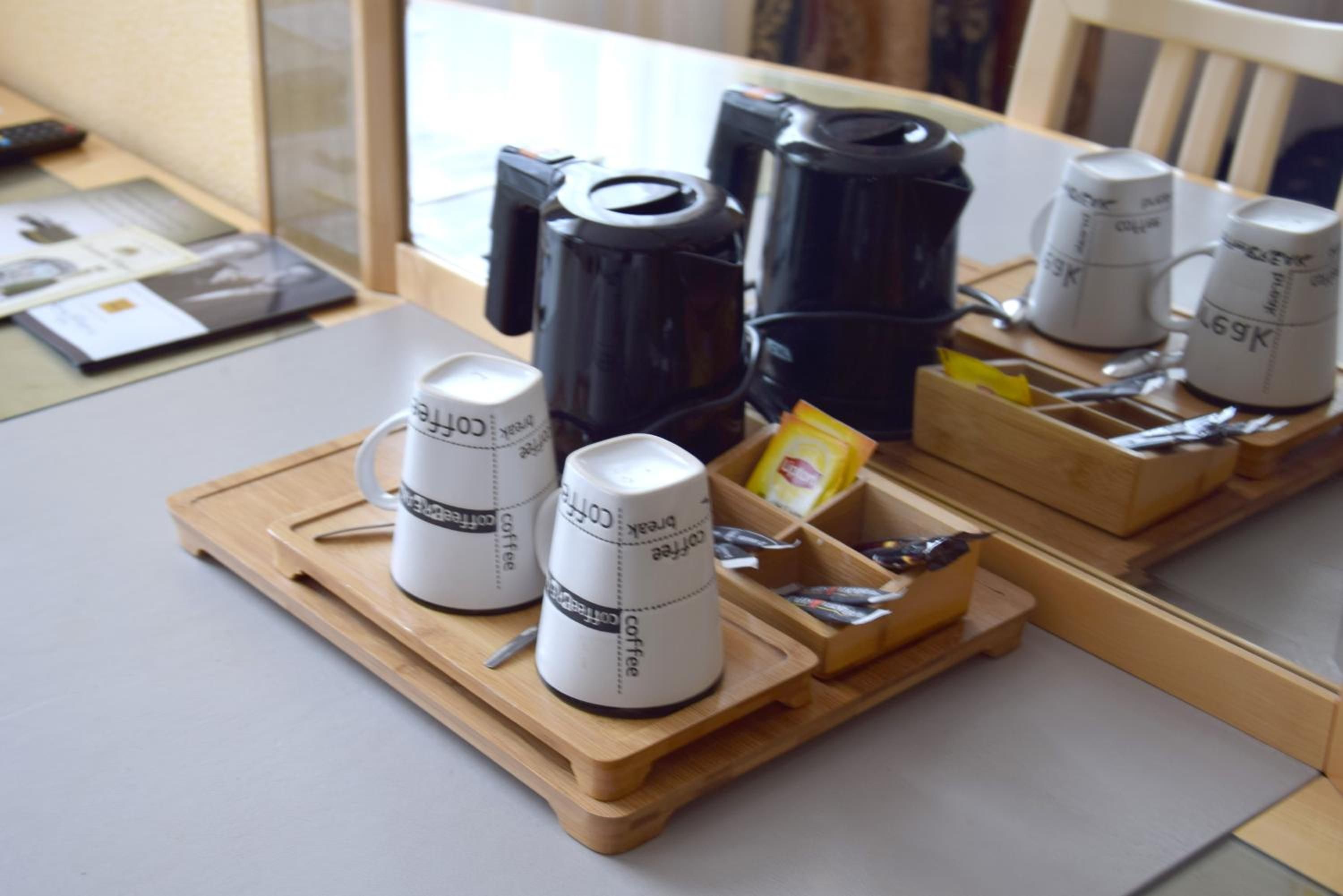 A table with coffee cups, a coffee maker, and a tray with utensils.