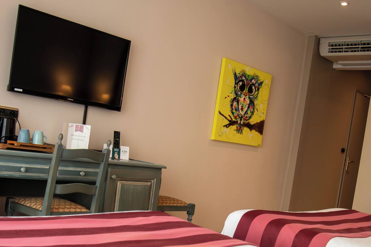 A hotel room with two beds, a desk with a chair, a flat-screen TV, and a painting on the wall.