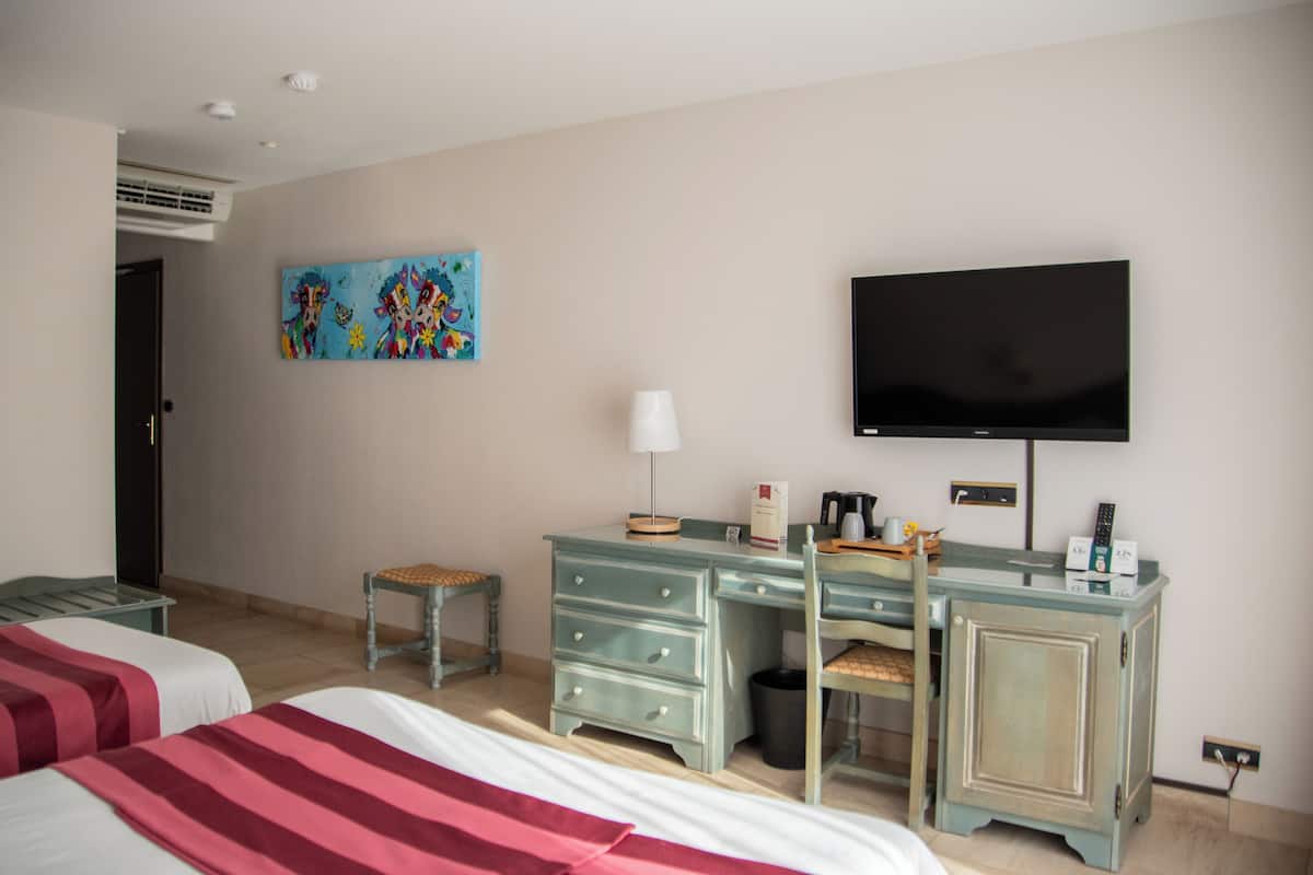 A hotel room with two beds, a desk, a chair, a television, and a painting on the wall.