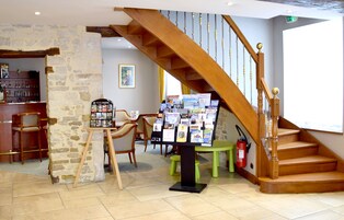 Un vestíbulo de hotel con una escalera de madera, una pared de piedra, un mostrador de recepción y un área de descanso con sillas.
