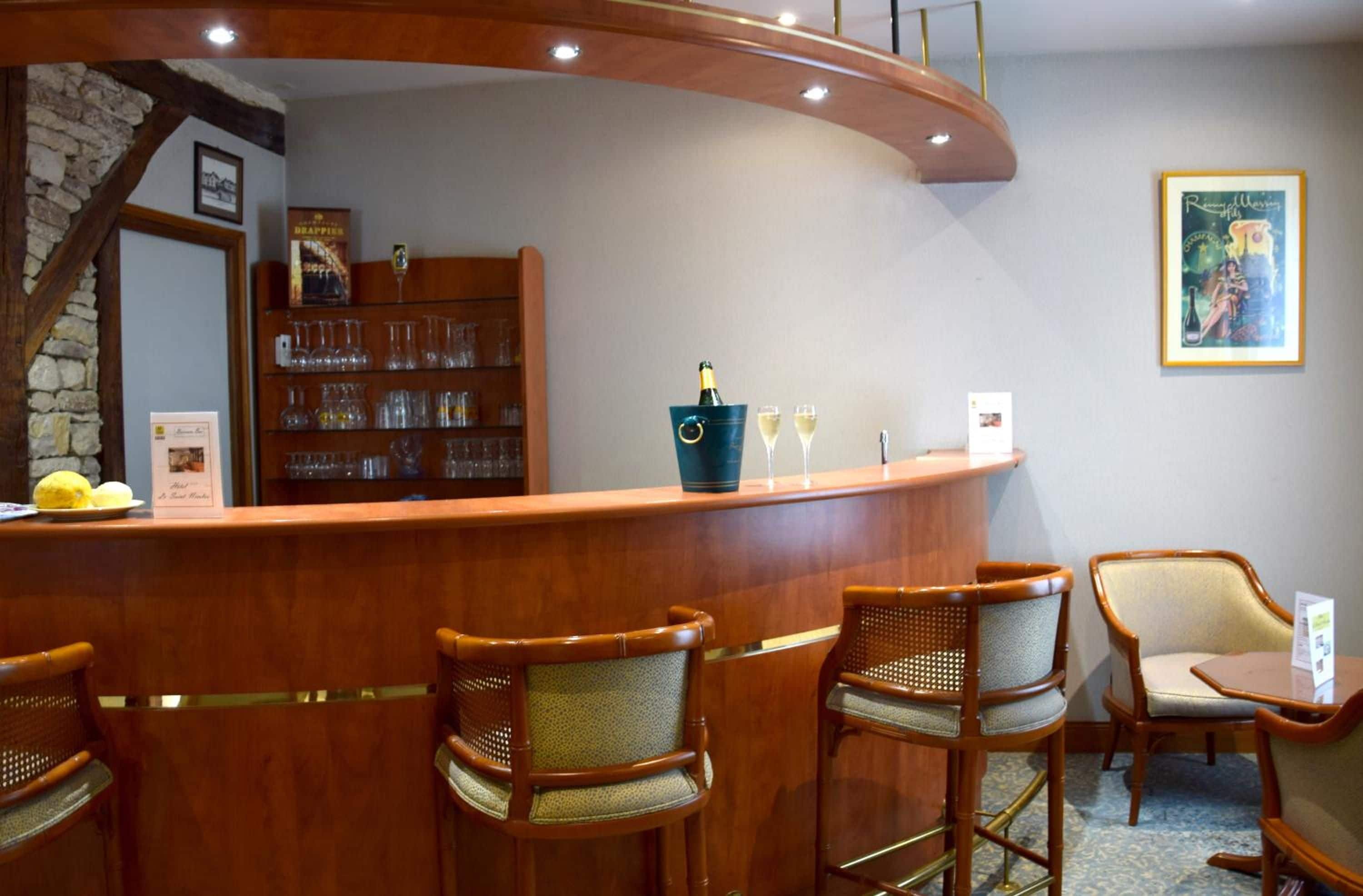 Zona de bar con una barra curva, sillas de madera y una estantería con cristalería.