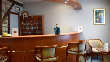 Zona de bar con una barra curva, sillas de madera y una estantería con cristalería.