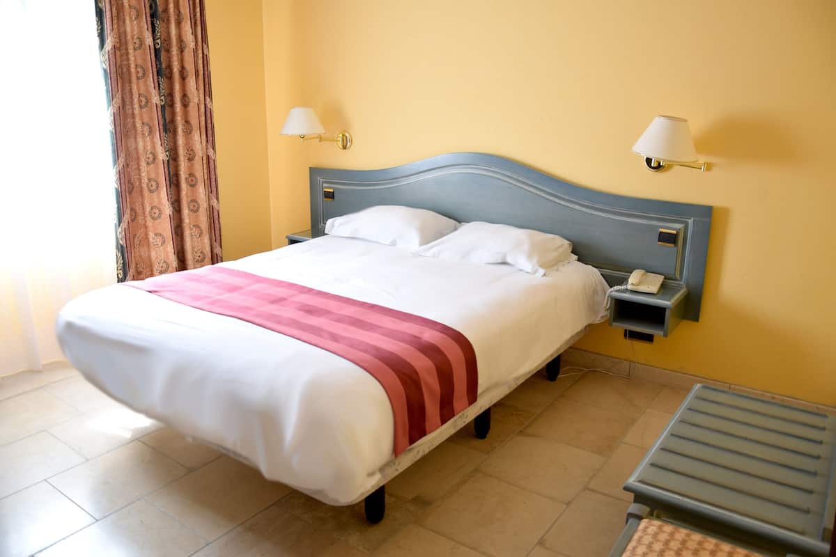 A neatly made bed with a white and red striped blanket, a bedside table with a lamp, and a telephone.