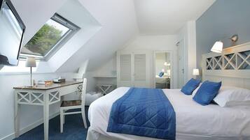 Une chambre d’hôtel avec une lucarne, un lit avec une literie bleue, un bureau et une chaise.