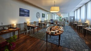 A spacious dining area with multiple tables and chairs, a large clock on the wall, and a view of the kitchen in the background. - Hotel Le Relais De Broceliande (Paimpont)