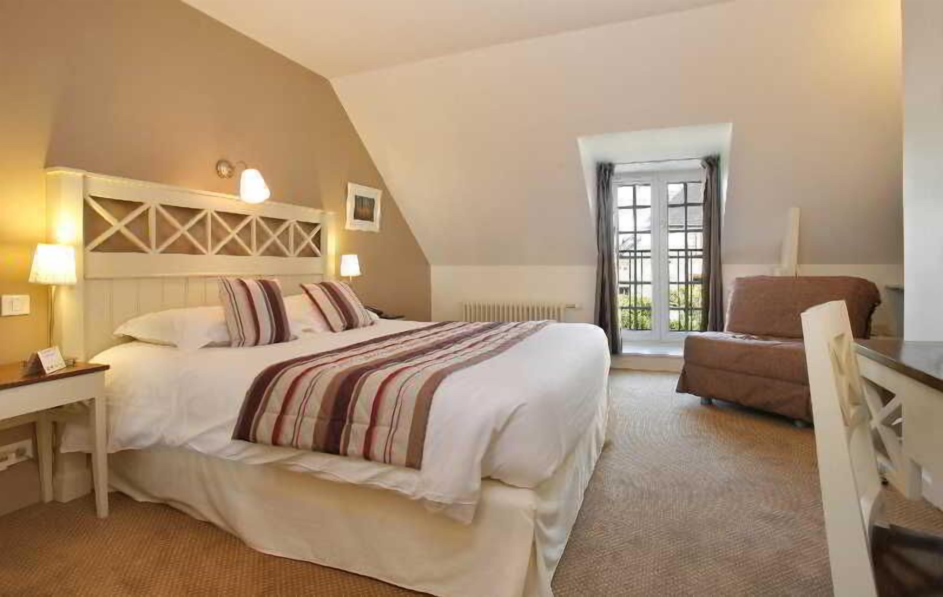 A hotel room with a bed, a desk, a chair, a radiator, and a window.