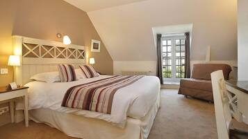 A hotel room with a bed, a desk, a chair, a window, and a radiator.