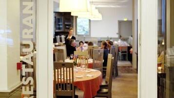 Un restaurante con mesas y sillas redondas, una zona de bar y una persona cerca de la entrada.