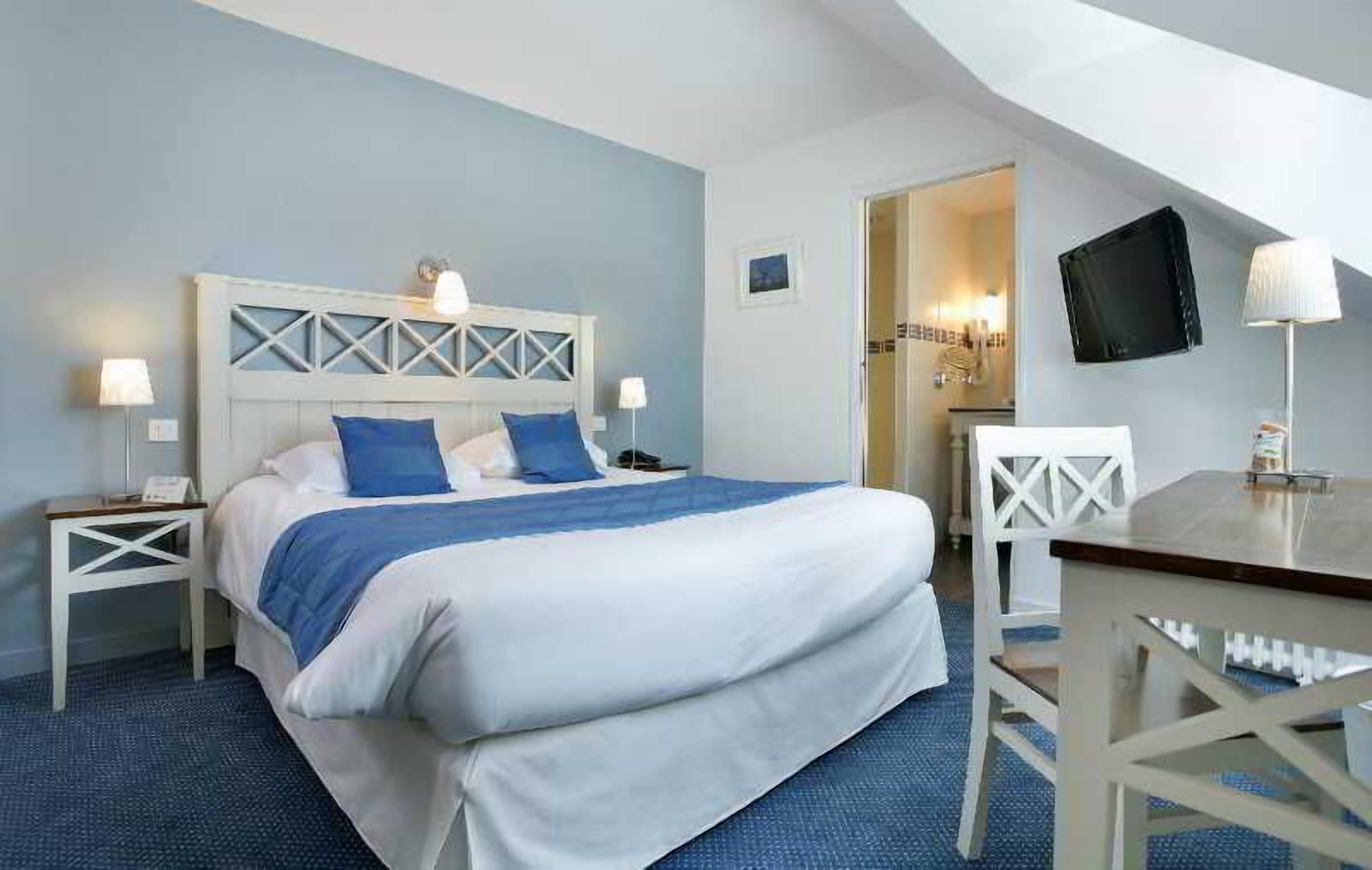 A bedroom with a bed, bedside tables, a desk, and a television.