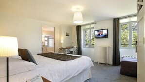 A hotel room with a bed, a desk, a television, and a window with curtains. - Hotel Le Relais De Broceliande (Paimpont)