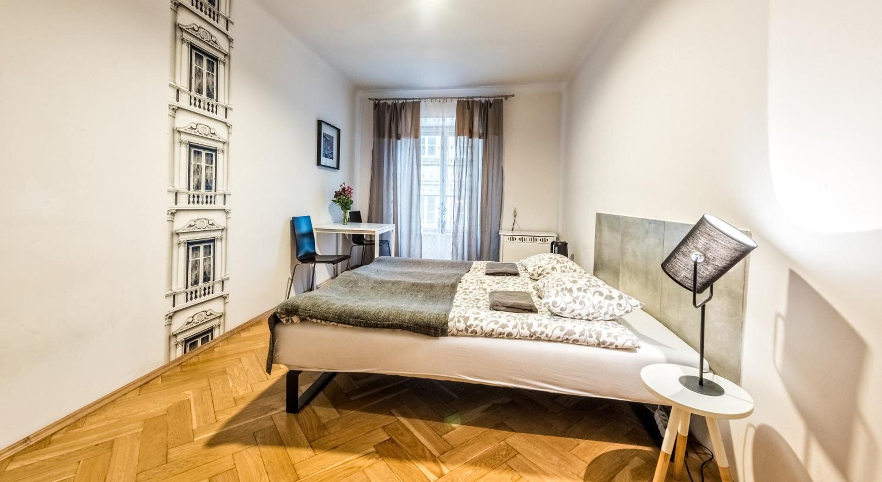 Un dormitorio con cama, escritorio, silla, lámpara y ventana con cortinas.