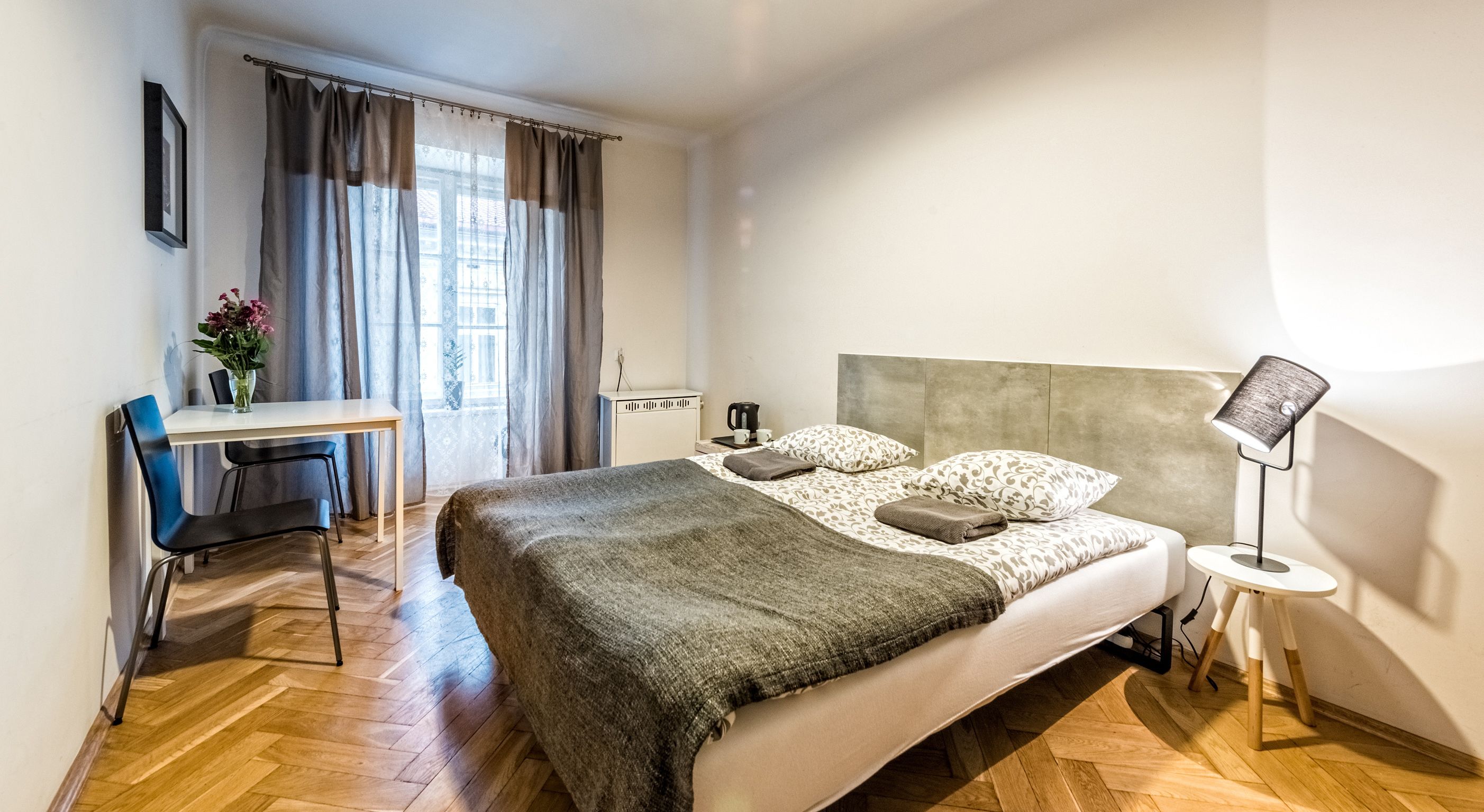Quarto de hotel moderno com uma cama grande, uma escrivaninha com cadeira, uma máquina de café e um abajur.
