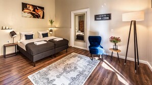 Un dormitorio moderno con una cama doble, un sillón azul, una lámpara de pie y un espejo decorativo.