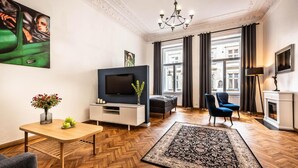 Una sala de estar moderna con piso de madera en espiga, televisor de pantalla plana, sofá, sillón azul, chimenea y un ventanal con cortinas.