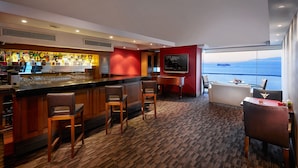 A bar area with a piano, seating, and a large TV screen. - Kordon Hotel Pasaport (Izmir)