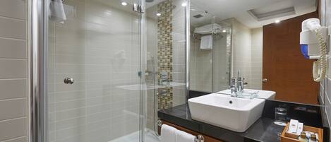Un baño moderno con ducha de vidrio, lavamanos blanco y tocador de madera.