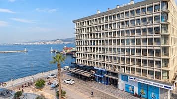 Un hotel de varios pisos con vistas al mar, un área de estacionamiento y un paseo marítimo con árboles y una fuente.