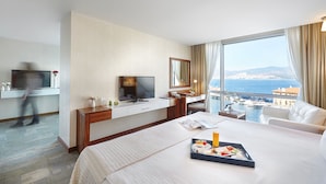 A hotel room with a bed, a desk with a TV, a large window with a view of the sea, and a breakfast tray on the bed. - Kordon Hotel Pasaport (Izmir)