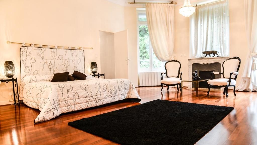 Un dormitorio con cama, dos sillones, chimenea y ventana con cortinas.