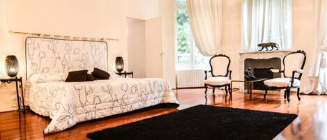 Un dormitorio con cama, dos sillones, chimenea y ventana con cortinas.