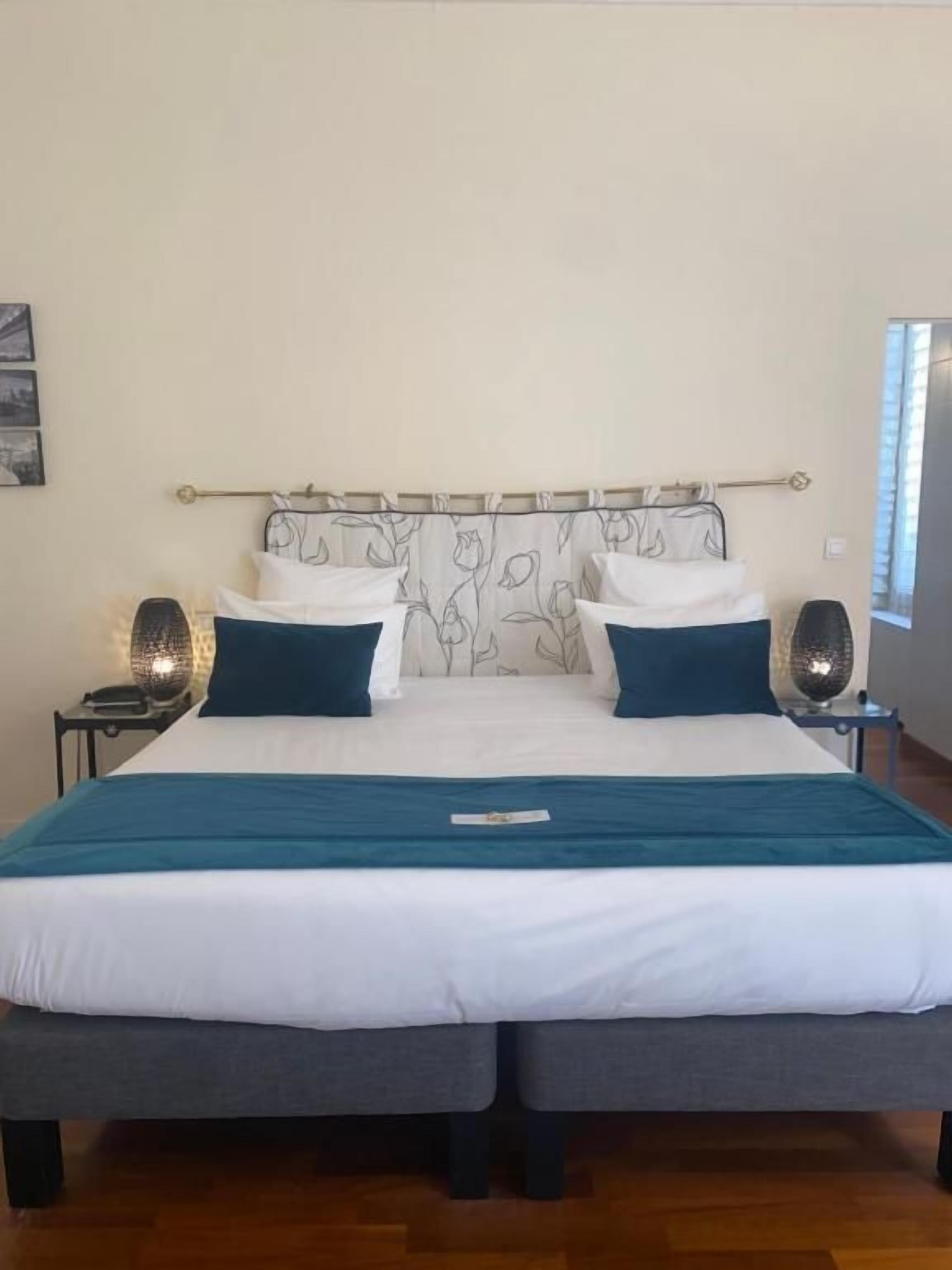 Una cama doble con cabecera, dos mesitas de noche y una ventana con cortinas.