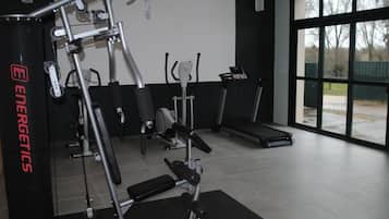 Academia com equipamentos de ginástica, esteira e uma grande janela.