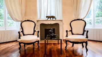 A room with two chairs, a fireplace, and a view of greenery through large windows.
