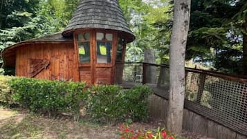A wooden cabin with a conical roof, surrounded by a fence and dense forest.