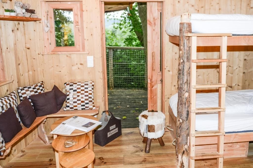 Una cabaña de madera con literas, un sofá con cojines estampados, una mesita y un taburete decorativo.