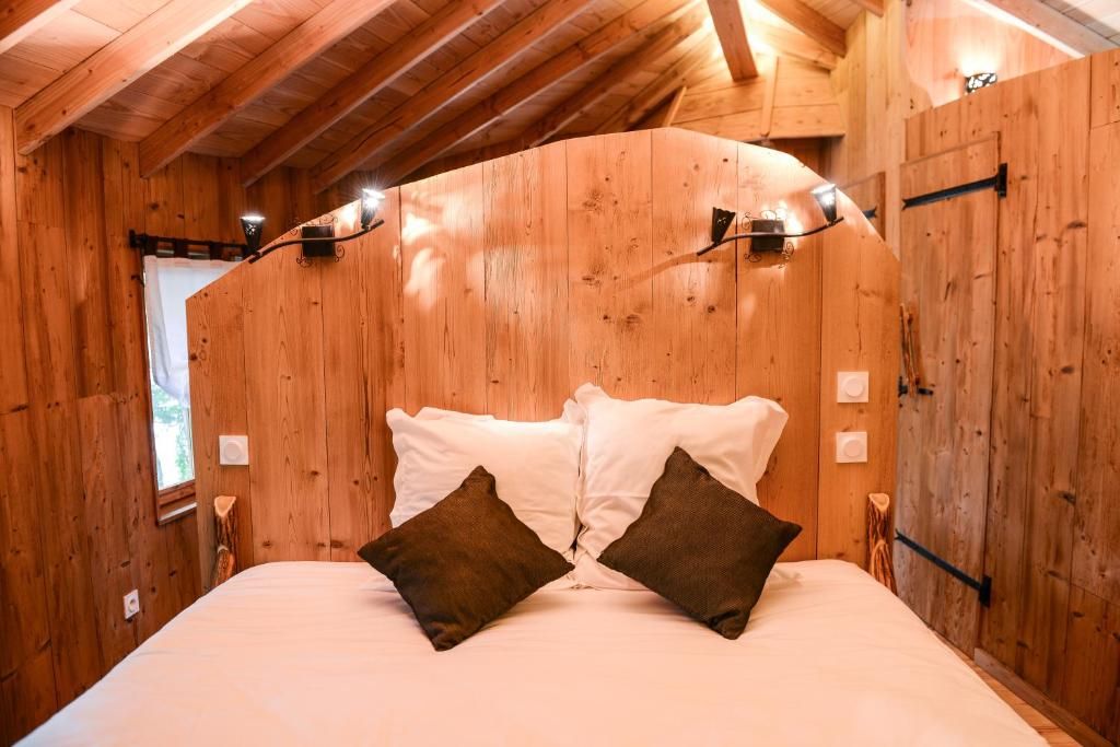 A wooden room with a curved ceiling, a bed with white bedding and two brown pillows, and wall-mounted lights.
