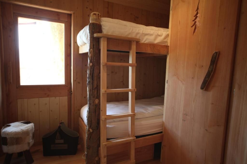 A bunk bed with a wooden ladder, a window with daylight, and a small stool.